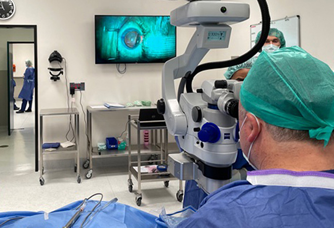 surgeon looking through microscope also displayed on a large screen wall monitor in operating room | Vision Hospital Group