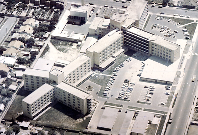 Aerial view of a multi-story hospital building surrounded by residential houses and a parking lot