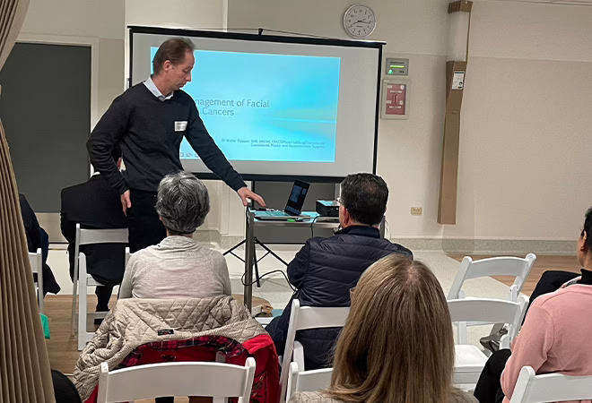A picture of a clinician presenting at AONA in Melbourne. He is pointing towards the bottom of the slide as he presents.