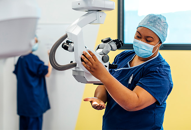 Director of Nursing, Kila Lua in scrubs adjusting position of operating microscope
