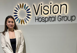 Margarette Cortez standing in front of an illuminated sign saying 'Vision Hospital Group'