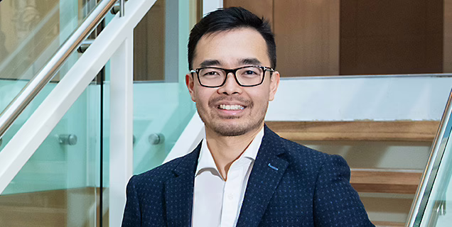 Dr Soo Khai Ng wearing a navy suit and white shirt and smiling at the camera.