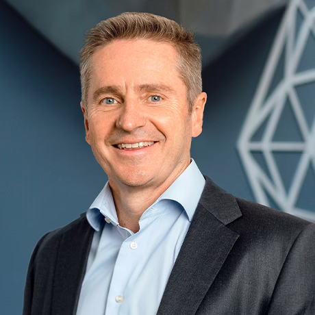 Headshot of Prof Gerard Sutton in a black suit and blue shirt (no tie) against a dark blue feature wall in Chatswood Day Surgery