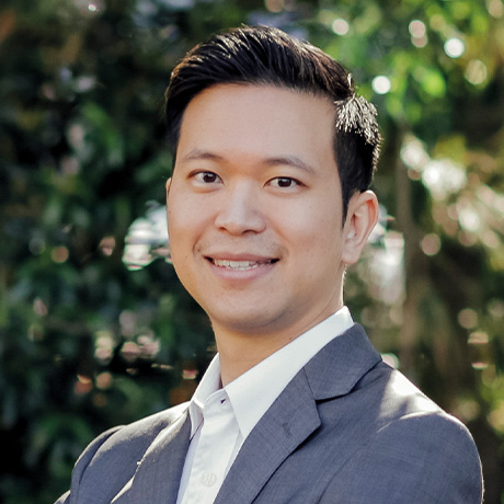 Outdoor headshot of Dr Jason Chang in a grey suit and white shirt in front of a hedge