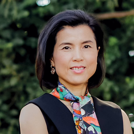 Headshot of Dr Tess Huynh in a sleveless black dress and multi-coloured, art-deco neck scarf outside Forest Road Day Surgery in front of bushes